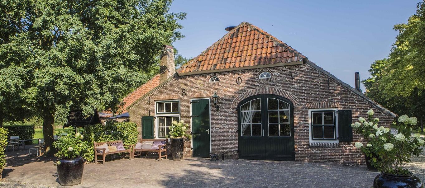 De voorkant van de hoeve met een landelijke uitstraling, laag breed en schuin dak en groene deuren